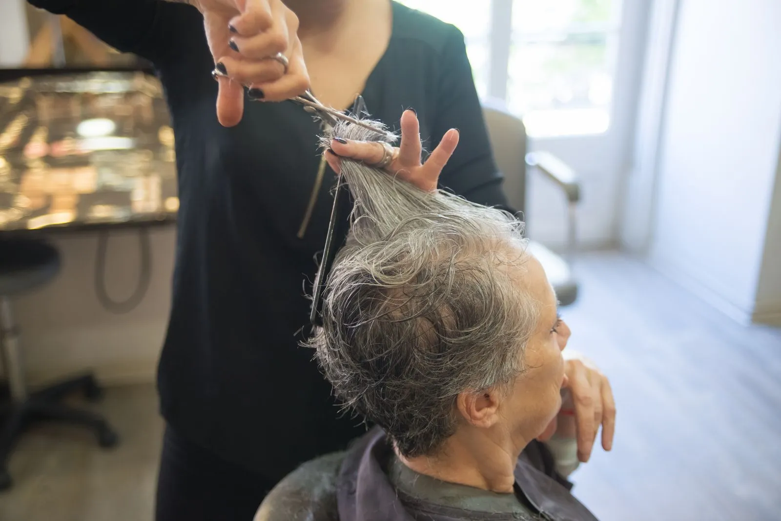 A hairdresser styles a senior woman's hair in an indoor salon setting.